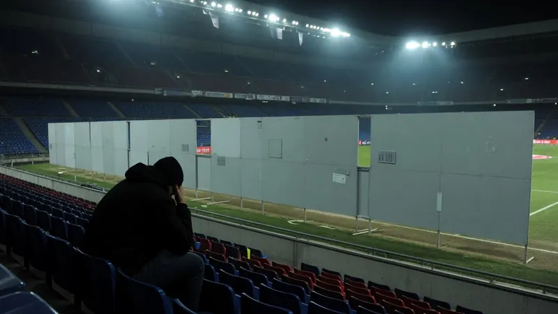A person in a black hoodie sits alone in stadium seats at night.